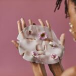 Woman about to apply a white face mask with a rose colored background