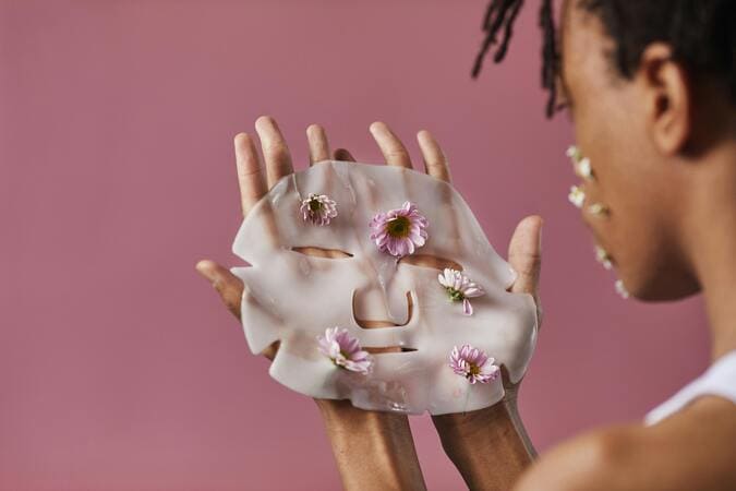 Woman about to apply a white face mask with a rose colored background
